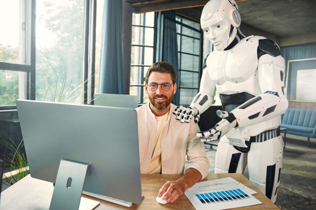 Image of a man working on a computer with a robot assistant in a futuristic office, showcasing the seamless integration of technology in the modern workplace.